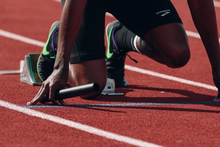 ランナーはトラックのスタート位置にいて、リレーのバトンを持ち、レースの準備を整えています。.