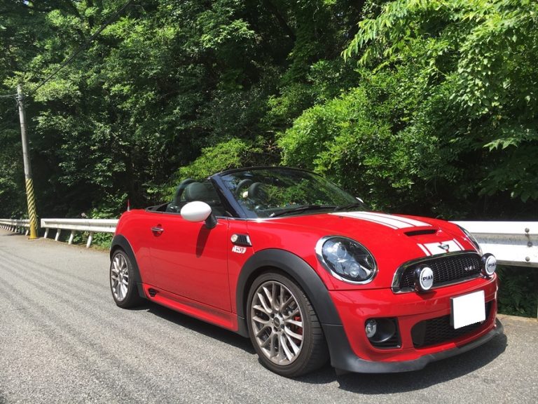 緑の木々と金属製のガードレールの隣の道路に駐車された赤いミニ クーパー コンバーチブル。.