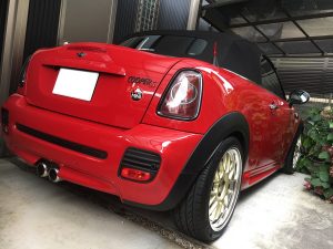 ガレージに駐車された、金色のホイールを装着した赤いMINI Cooper Sコンバーチブルを、運転席側後方から見たところ。.