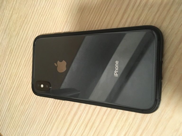 ケースをつけた黒い iPhone が、明るい色の木製の表面の上に表面を下にして置かれています。.