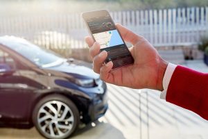 日光の下で駐車した黒い車の近くに、地図アプリを表示したスマートフォンを持った人がいます。.