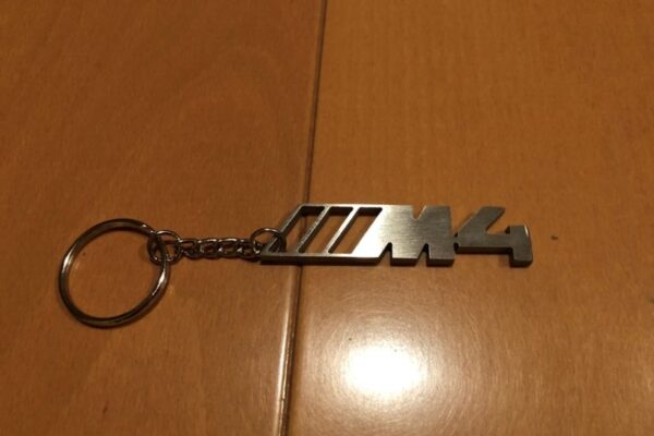 木製の表面にM4のロゴが入った金属製のキーホルダー。.