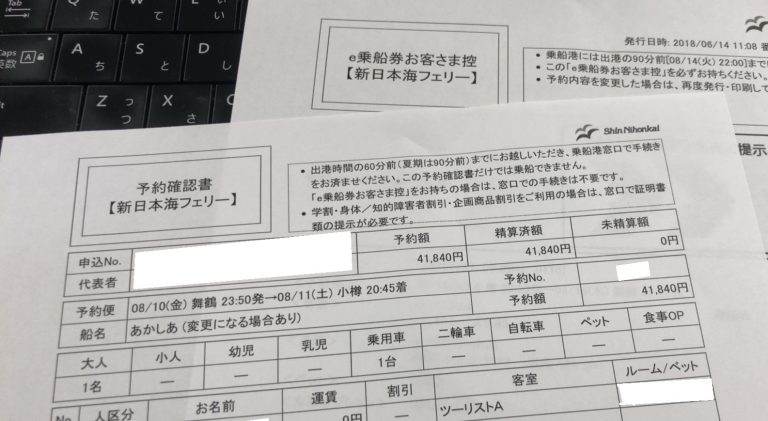 黒いコンピューターのキーボードの横の机の上にある日本のフェリーの予約フォームのクローズアップ。.