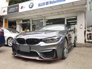 BMWの看板のある自動車店の前に、赤いトリムが付いた灰色のBMWスポーツカーが駐車されています。.