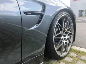 建物の近くの路上に駐車された、灰色の BMW M4 の前輪とフェンダーのクローズアップ。.