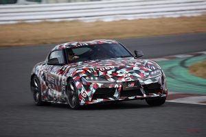 カモフラージュされたスポーツカーが、ぼやけた背景とダイナミックな動きで、レーストラックで急カーブを曲がっています。.