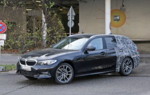 太陽の壁画がある建物の近くの路上に、リアに迷彩ラップが施された黒い BMW ワゴンが駐車されています。.