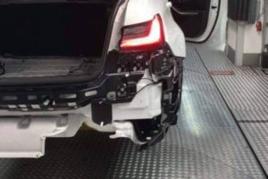 ガレージに置かれた、リアバンパーが損傷し、内部部品が露出した白い車。.