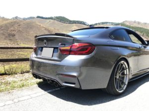 丘と木々を背景に、道路脇に駐車された銀色の BMW M4。.