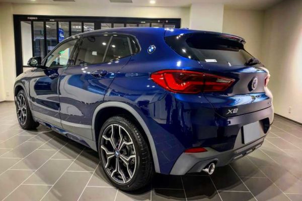 青い BMW X2 SUV が屋内のタイル張りの床に駐車されており、後ろ側から見ています。.
