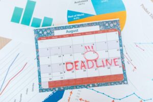 8 月を示すカレンダー。赤いマーカーで DEADLINE と書かれており、その周囲にはさまざまなチャートとグラフが配置されています。.