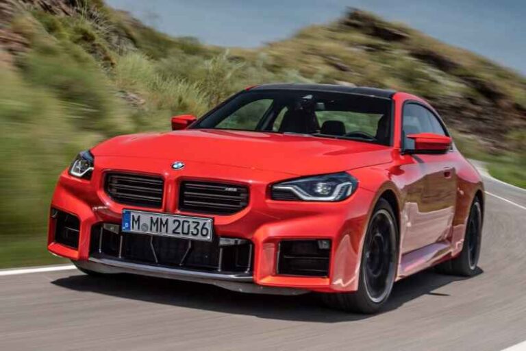 緑を背景に曲がりくねった道を走る赤い BMW スポーツカー。.