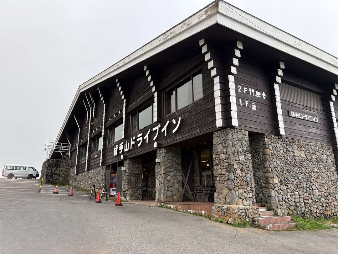 横手山ドライブインの外観。石造りの柱と黒い木壁が特徴的な建物。