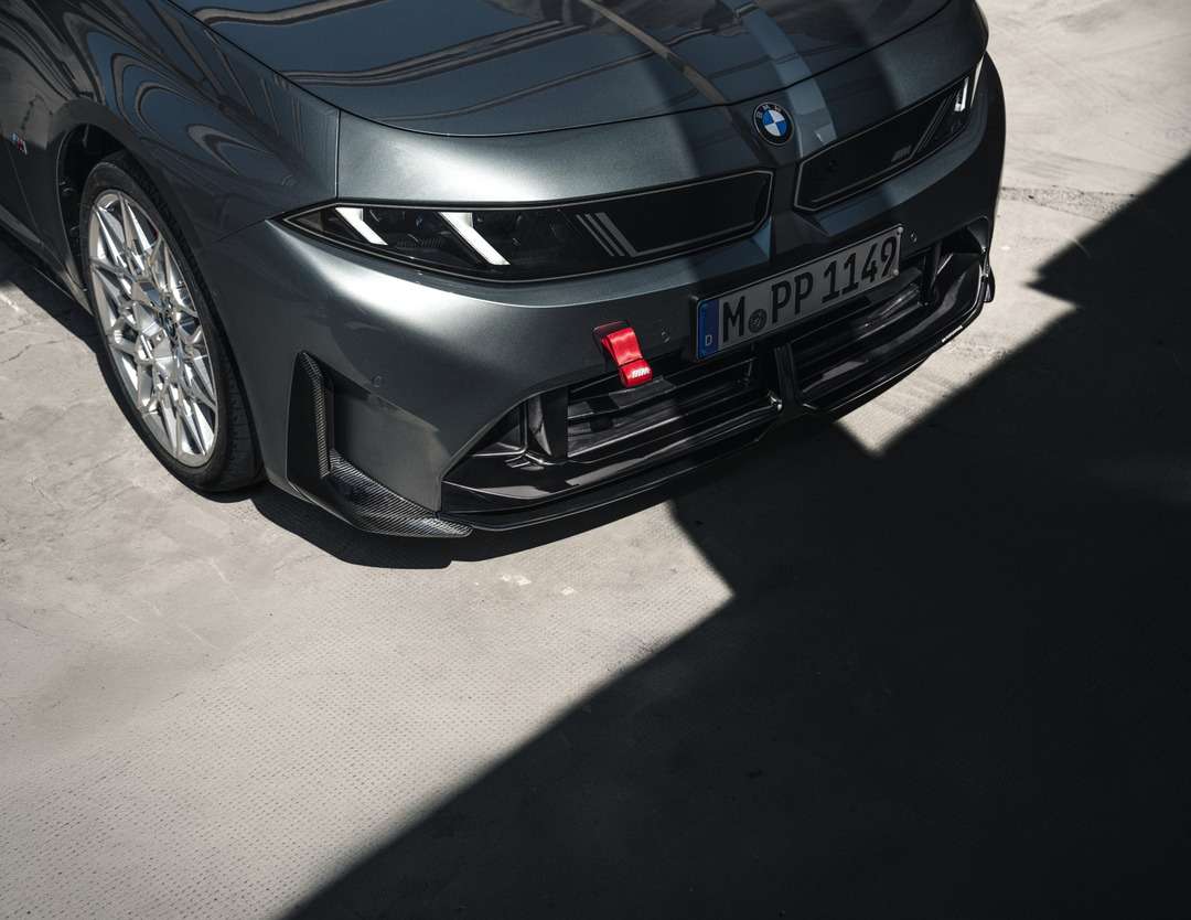ダークグレーのBMWのフロント部分。鋭いヘッドライトと赤い牽引フックが見える。